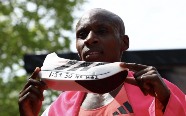 Kenya's Sabastian Sawe celebrates with a shoe after winning the men's elite race and setting a new world record with a time of 01:59:30