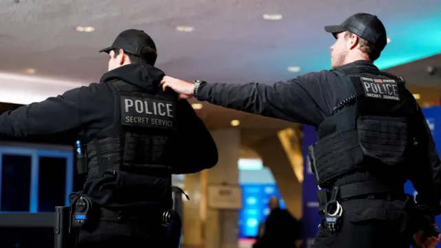 Two Secret Service officers stand with their backs to the camera with 'Police' marked on their uniforms