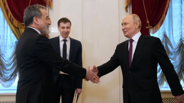 Araghchi and Putin, both wearing dark suits, walking towards each other and shaking hands.