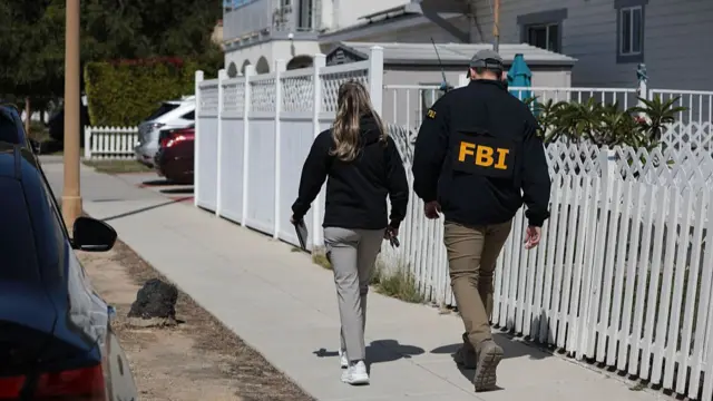 Two FBI officers walk through a white picket fence estate in Torrance, California.