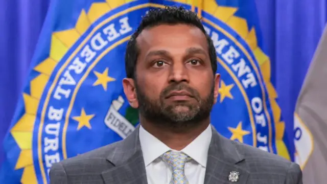 A man in a grey suit and tie and white shirt in front of the seal of the FBI