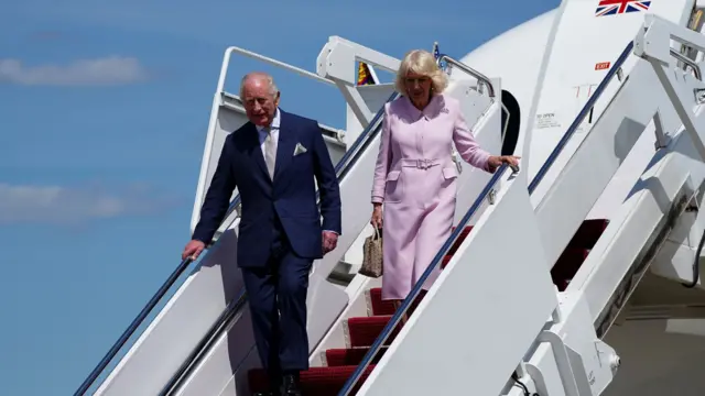The King and Queen descend the stairs from the plane