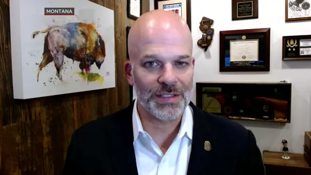 Retired FBI special agent Daniel Brunner speaking into a camera on Zoom, with a painting of a moose on a wall behind him and certificates on the perpendicular wall