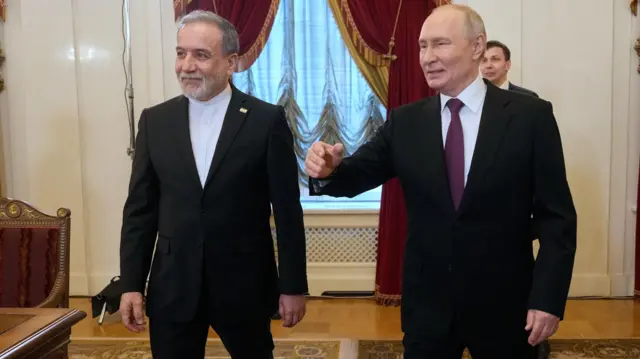 Abbas Araghchi stands in a dark suit next to Vladimir Putin