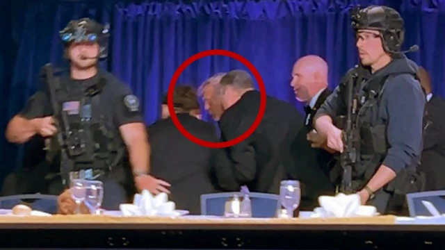 President Trump is evacuated by the Secret Service during the incident. He is surrounded by men in suits, and two men with guns stand in the foreground.