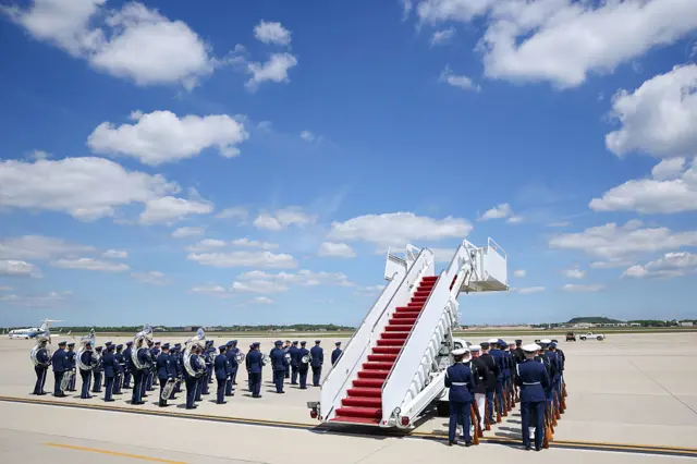The US Army band and honor guard prepare ahead of the arrival. A set of stairs is ready for when the plane lands