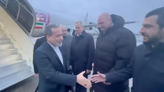 Aragchi wears a dark suit and white shirt as he shakes hands with officials