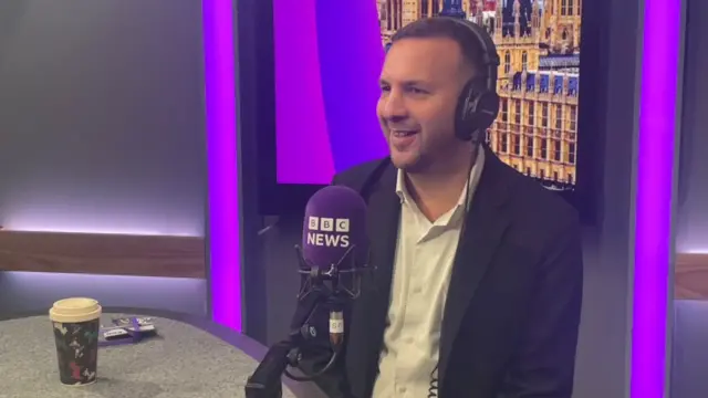 Zack Polanski in a radio booth wearing headphones and sitting in front of a microphone