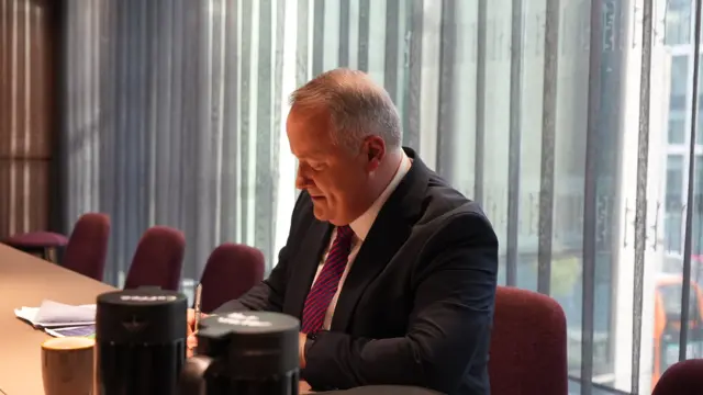 Darren Millar sits at a desk making notes.