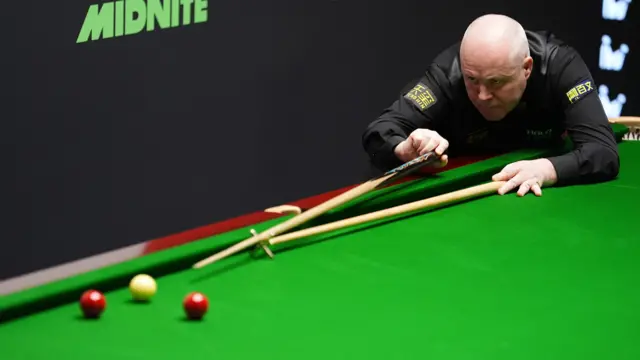 John Higgins plays a shot with the rest