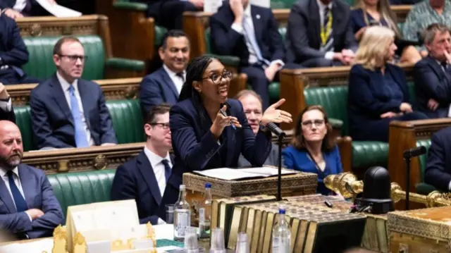Badenoch stands in the House of Commons with her arms slightly raised as she makes a point
