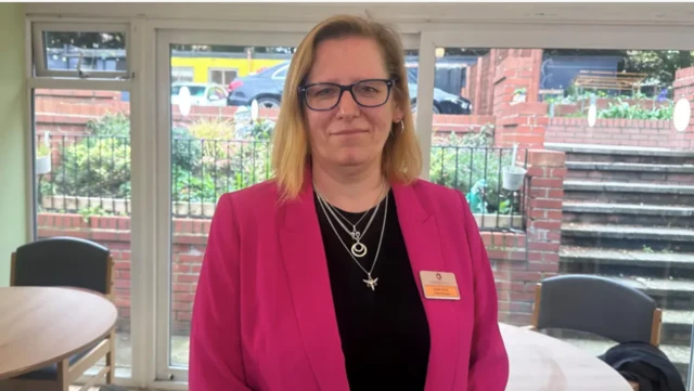 Alena Petrie has blonde shoulder-length hair and is wearing a black top, with four silver necklaces and a bright pink jacket.