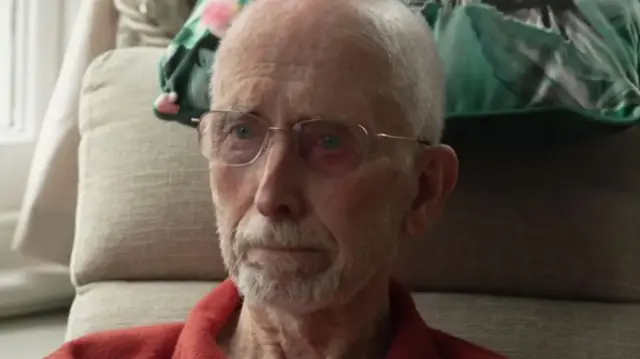 Brian Gundry has short grey hair and a beard. He is sitting in a beige armchair.