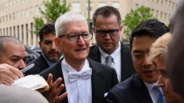 Apple CEO in white tie surrounded by a group of men in suits