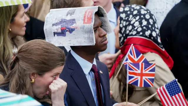 A man is pictured wearing a suit looking tired. There is a wet copy of The Economist on his head, presumably to shield himself from rain.