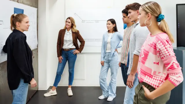 A woman guides her classmates through a project on a whiteboard