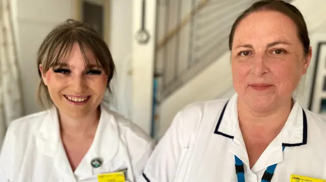 Laura Mills is smiling at the camera and is wearing a white uniform. Debbie Smith has brown hair, in a ponytail, and is also wearing a white uniform.