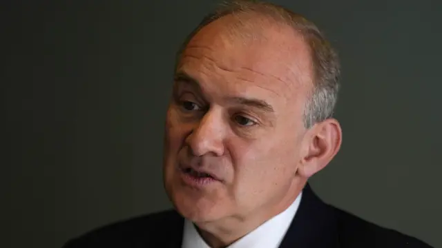 Sir Ed Davey looks at the camera to the side and is wearing a suit and white shirt.