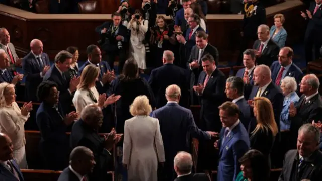 Queen Camilla and King Charles walking through a crowd of people in the House of Representatives.