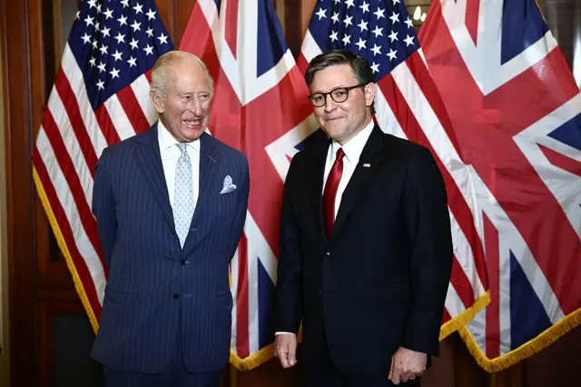 Two men in suits stand in front of a display of US and UK flags