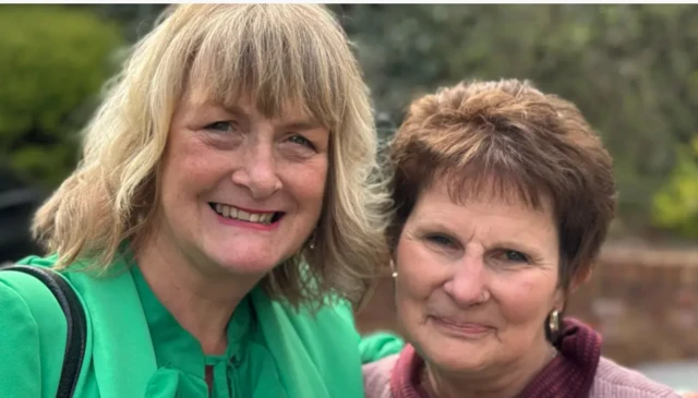 Ali France has blonde wavy shoulder-length hair and is wearing a bright green jacket and top. She has her arm round Sarah Forsyth, who has a nose ring and gold earring and has short brown hair.