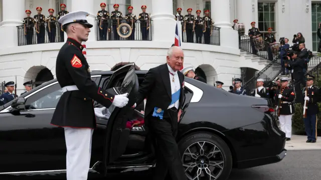 King Charles III gets out of a black car, which is held open by a US Military Guard.