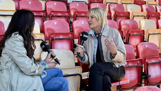 Two women sit inside a football stadium with red and yellow seats