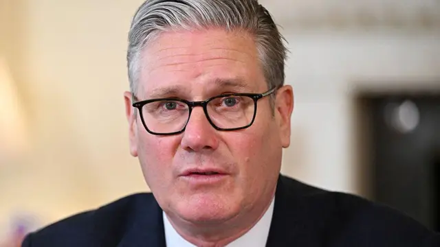 Sir Keir Starmer wearing a dark-coloured suit and black-rimmed glasses. He has short, grey hair.