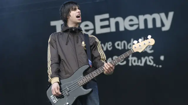The Enemy in front of a backdrop saying their name, performing on stage