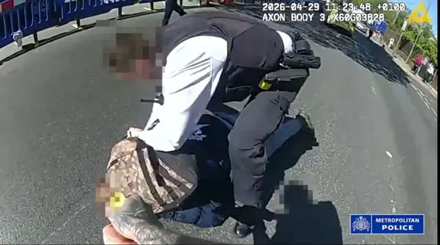 An officer can be seen crouched over a suspect in an attempt to restrain him. The faces of both have been blurred