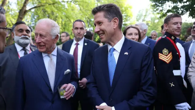 King Charles III and Sir Christian Turner smiling and looking around at a garden party at the British Embassy in Washington DC, surrounded by many other guests