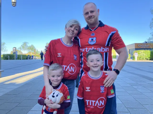 A family with a mum, dad and two small boys all in York kits smile for the camera