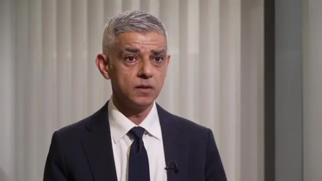 London Mayor Sadiq Khan in a dark suit and tie against a beige background.