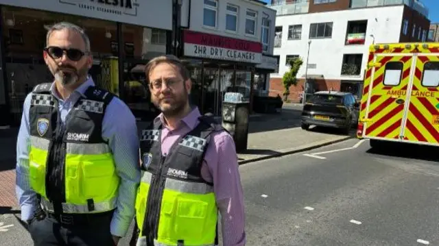 Two men standing with security vests near an ambulance.
