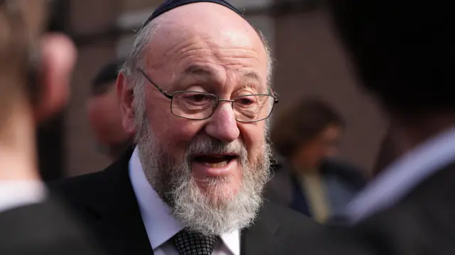 Sir Ephraim Mirvis pictured wearing a black suit, white shirt and black tie in a crowd