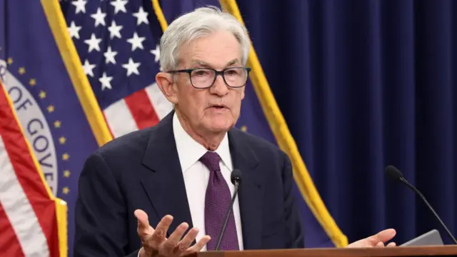 Jerome Powell gestures in front of a backdrop of flags