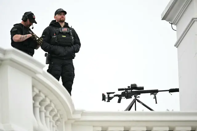 US Secret Service standing on what looks like a roof behind the white balcony edge with a sniper
