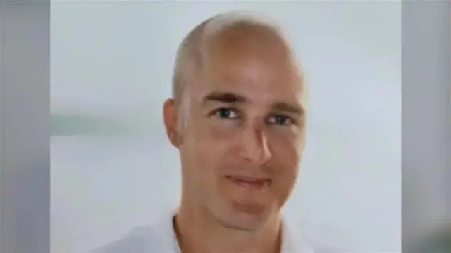 A bald man. He is smiling and wearing a white polo shirt.