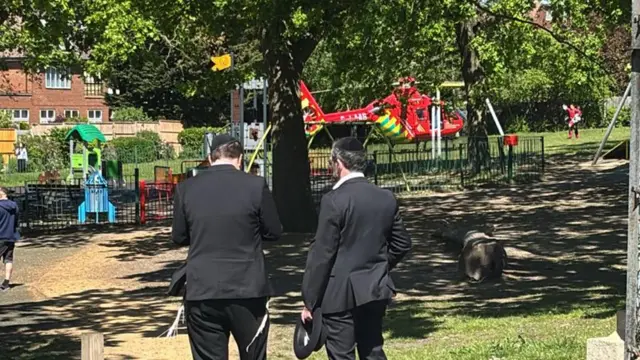 An air ambulance appears to have landed in a park area. Two men stand in the foreground of the image