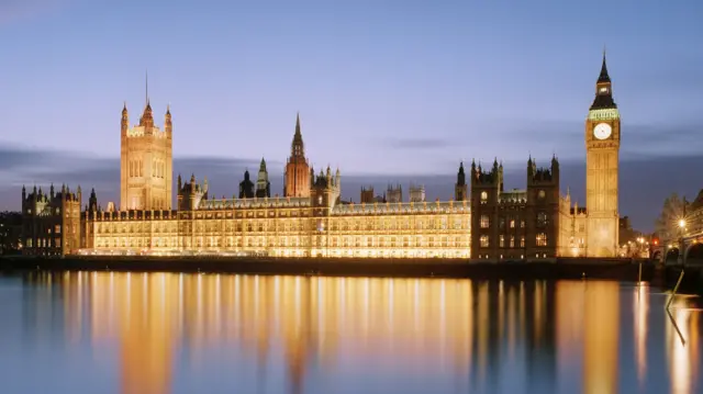 Panoramic view of Houses of Parliament and Westminster Bridge reflected in River Thames at dusk.