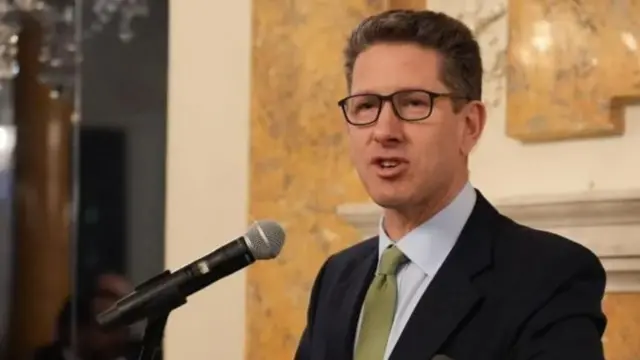 Sir Christian Turner speaking on a podium wearing a suit and glasses