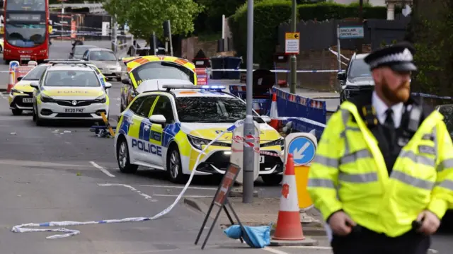 A police officer standing in the foreground of a police cordon.