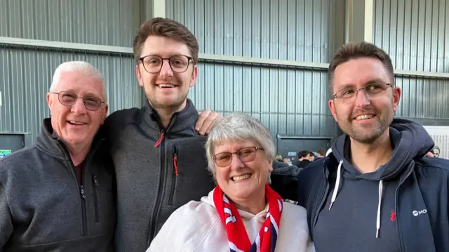 Three men and one woman stand with their arms around each other