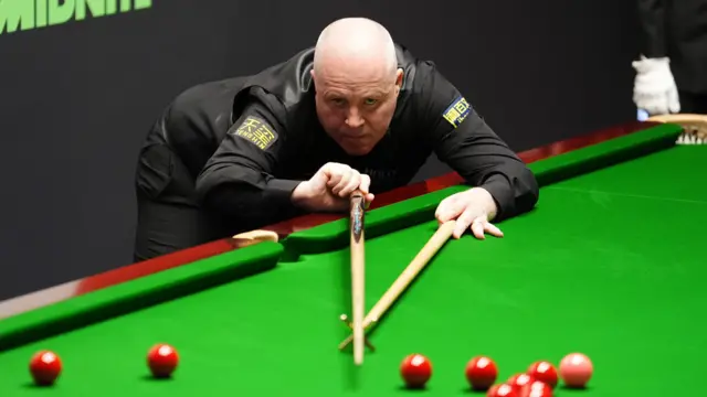 John Higgins plays a shot with the rest