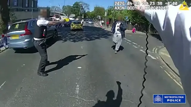 An outstretched arm of an officer is in the right hand side of the shot. The suspect appears to be approaching. Another officer is to the left. Faces have been blurred