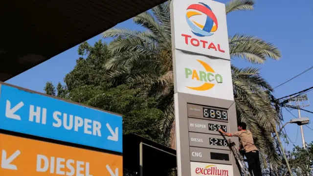 A man works to change the numbers on a price board at a petrol station