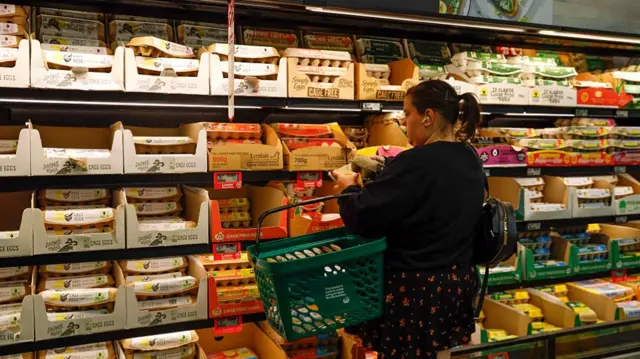 A woman with a basket picks up an egg tray at the supermarket