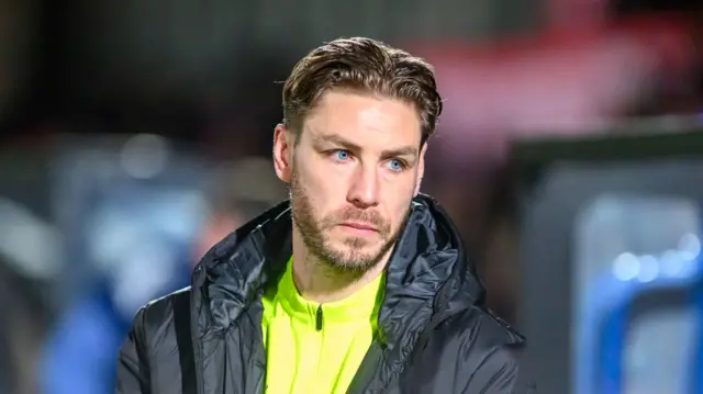 A close up of Barrow's interim boss Sam Foley wearing a neon yellow jumper and a black hooded jacket