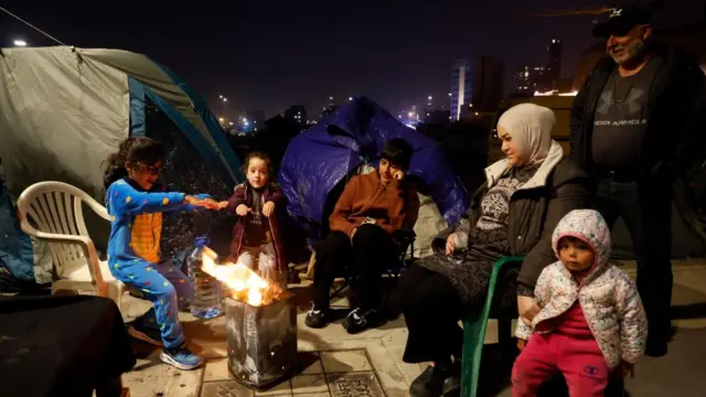 Internally displaced Lebanese residents warm themselves around a fire at a makeshift camp in the waterfront area of Beirut