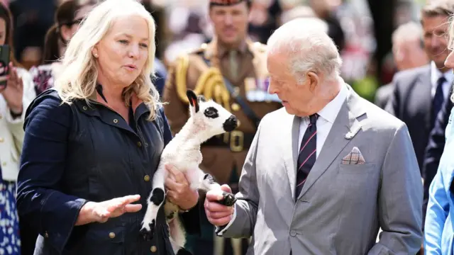 King Charles holds the hoof of a lamb, which is in the arms of its keeper